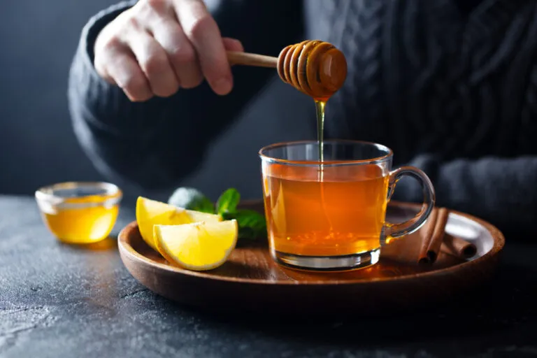 Cup,Of,Tea,With,Pouring,Honey,And,Lemon.,Grey,Background.