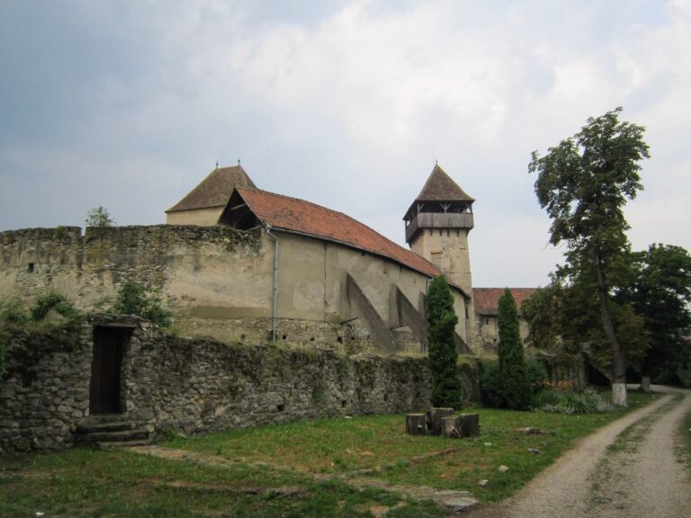Biserică fortificată cu ziduri de apărare și turn înalt, înconjurată de casele colorate ale unui sat transilvănean