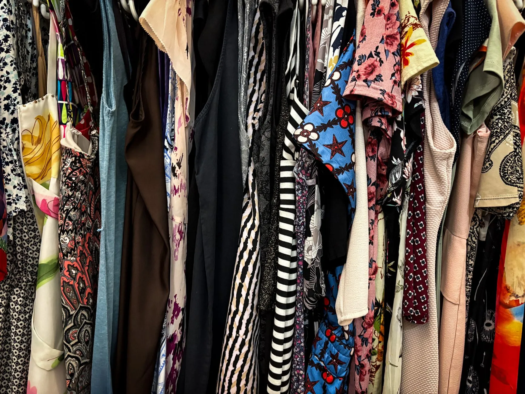Rochii în stil retro, cu imprimeuri cu buline și flori, așezate pe un stand de haine într-un atelier luminos